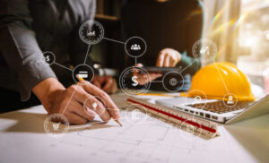 Two colleagues, data and money icons, tablet and laptop on desk in office.
