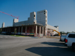 Modern Concrete Building Under Construction With Scaffolding And Crane Against Clear Blue Sky.