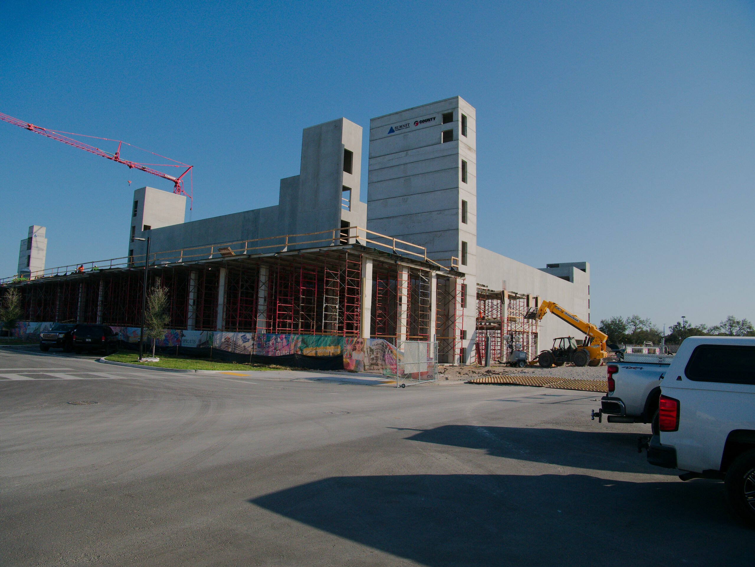 Modern Concrete Building Under Construction With Scaffolding And Crane Against Clear Blue Sky.