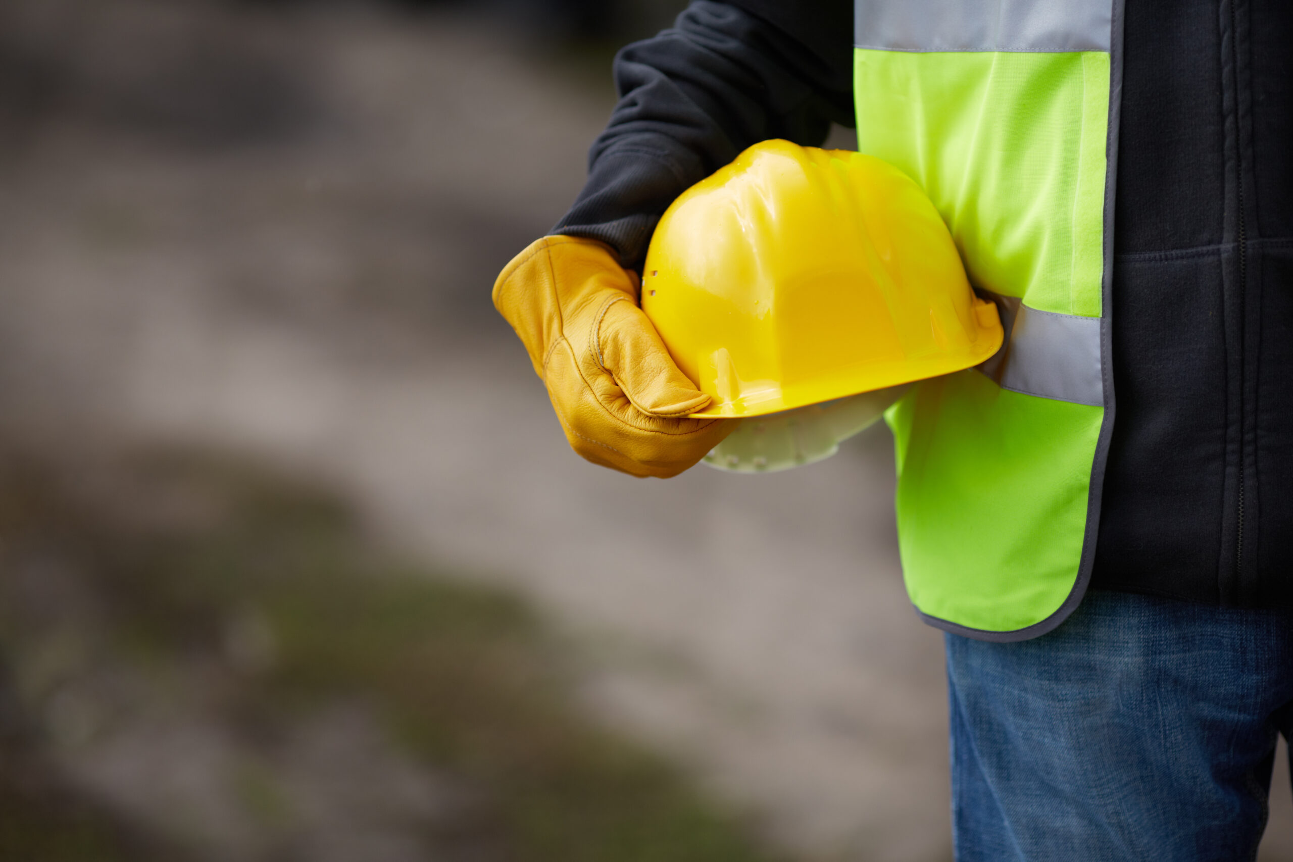 Builder with yellow helmet and working gloves on building site.