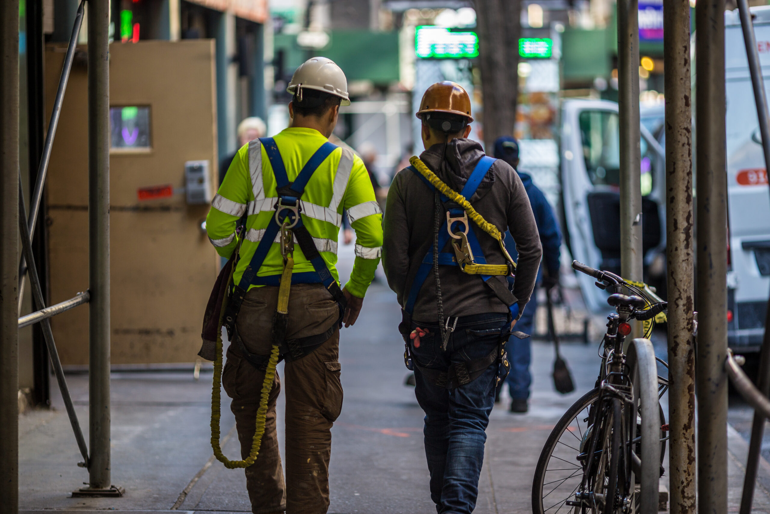 Two construction workers walk together down a New York City sidewalk.