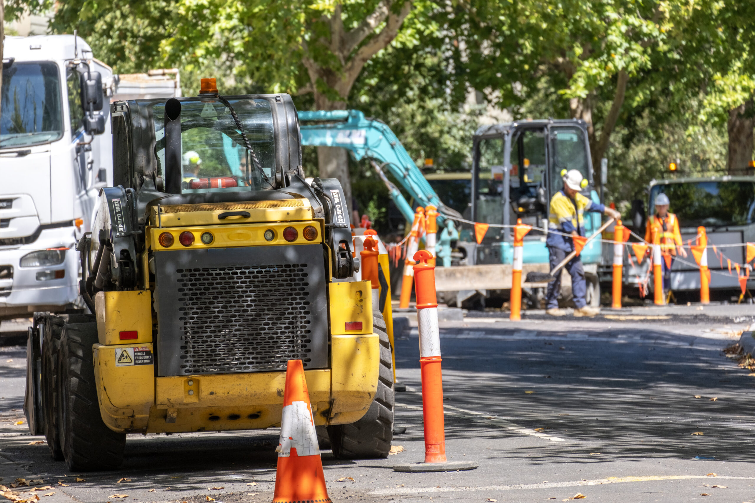 Road construction work in progress on an urban street with a road roller and workers in safety gear installing new asphalt.