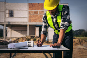 architect in safety vest and hard hat inspecting blueprint for building construction project